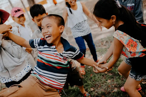 Little boy laughing as a circle of kids pull on his arms and legs